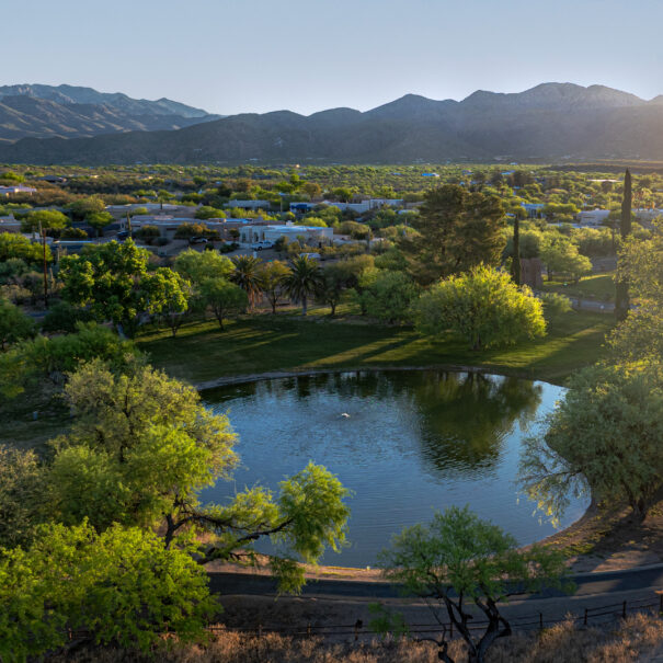 Aerial view of a circular pond surrounded by trees, set against a backdrop of mountains and a setting sun, just beyond the renowned Forty Niner Country Club bar.