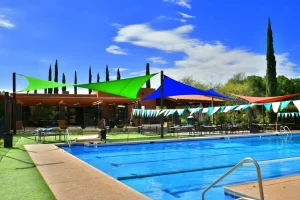 The swimming pool at forty niner country club surrounded by a grassy area with colorful shade sails and string lights. There are tables and chairs set up nearby.